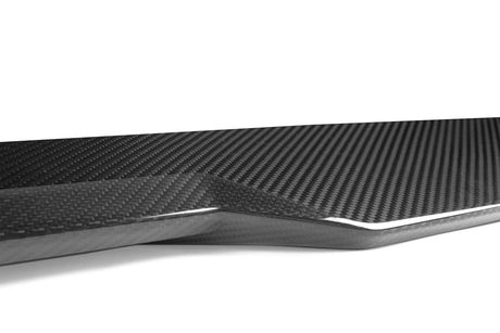 A sleek carbon fiber piece, displaying a glossy, woven texture, rests on a plain white background, emphasizing its modern design and intricate pattern.