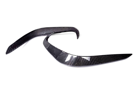 Two curved carbon fiber pieces are positioned parallel on a white background, likely automotive parts, showcasing sleek, aerodynamic lines and a glossy finish.
