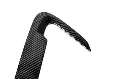 A glossy, black carbon fiber part with a sharp, angular design against a white background, showcasing its sleek texture and modern appearance.