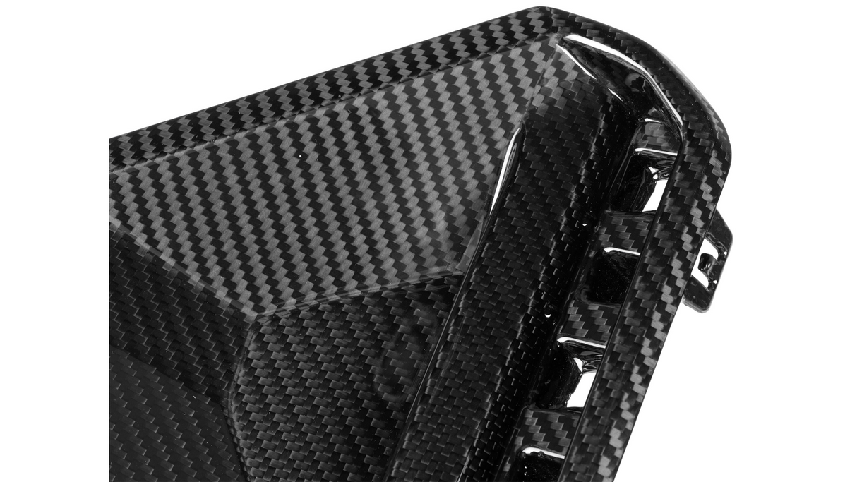 A close-up of a glossy carbon fiber object, likely a car part, with a woven pattern and angular design, featuring small vents or openings along the edge.
