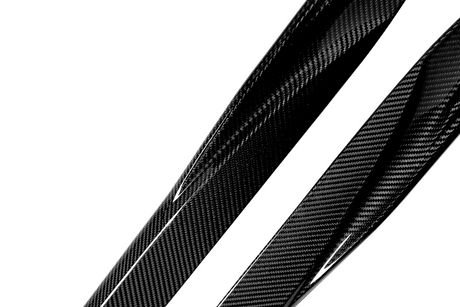 Glossy carbon fiber strips with a distinctive woven pattern lie diagonally on a white background, reflecting light and emphasizing their texture and sleek appearance.