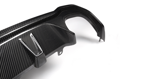 A carbon fiber car part with angled attachments lies on a plain white background, showcasing its textured surface and precision design.