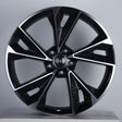 A black and silver alloy wheel with a geometric design and five dual spokes is displayed upright on a neutral background. The center features a logo with four interlocking rings.