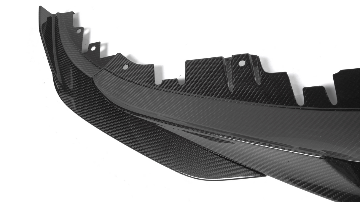 A carbon fiber car panel with textured surface and notched edge lies on a plain white background, showcasing detailed craftsmanship and modern design elements.