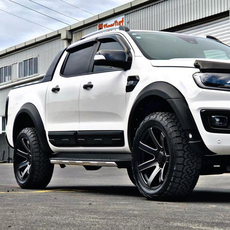A white pickup truck with large black wheels is parked in front of a corrugated metal building under overcast skies. A sign on the building reads "FleetFirst."