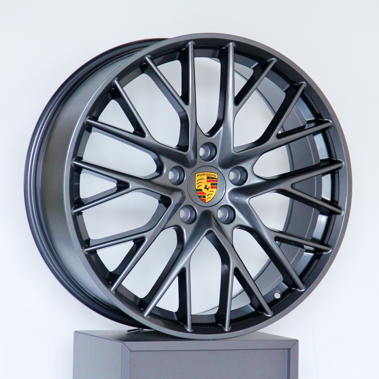 A dark alloy wheel with a multi-spoke design and a central Porsche logo is displayed upright against a plain white background.