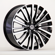A car wheel features a black and silver multi-spoke design with a central Volkswagen emblem, displayed against a plain white background.
