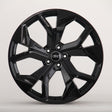 A shiny black, multi-spoke alloy wheel with an "Audi" emblem in the center is displayed against a plain, light gray background.