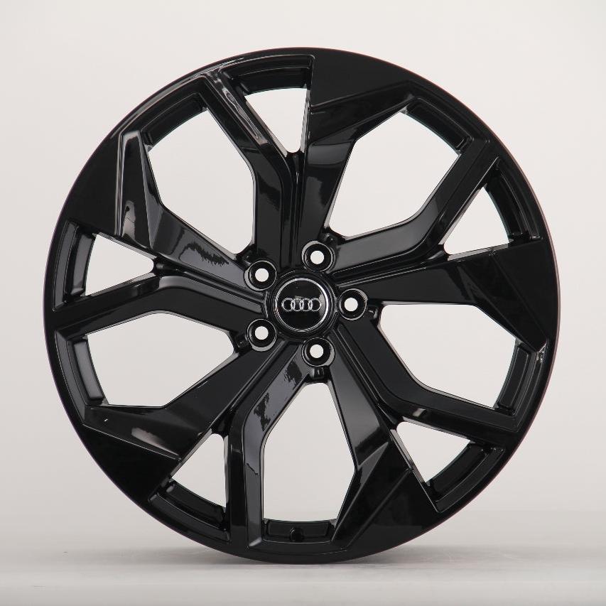 A shiny black, multi-spoke alloy wheel with an "Audi" emblem in the center is displayed against a plain, light gray background.