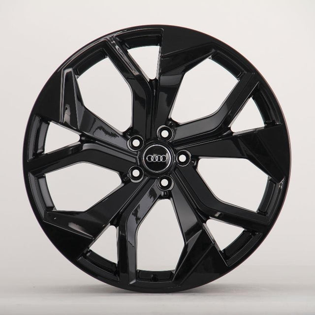 A shiny black, multi-spoke alloy wheel with an "Audi" emblem in the center is displayed against a plain, light gray background.