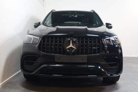 A black Mercedes-Benz SUV with prominent front grille and star emblem is parked indoors, against a plain white wall, on a tiled floor.