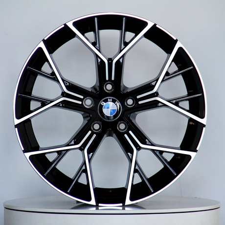 A black and silver BMW alloy wheel, featuring a multi-spoke design, is displayed upright on a light gray circular platform. The BMW logo is centered.