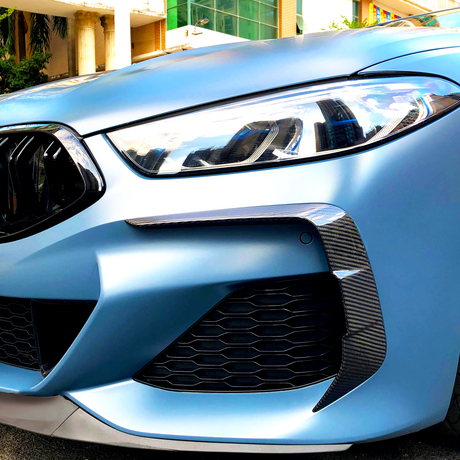 A sleek car front features angular headlights and a sporty grille, parked in an urban environment with modern buildings in the background.