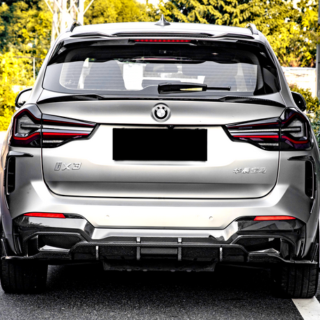 Silver SUV parked on pavement, displaying sleek taillights and glossy finish; marked with "iX3" and Chinese characters, surrounded by lush green foliage.