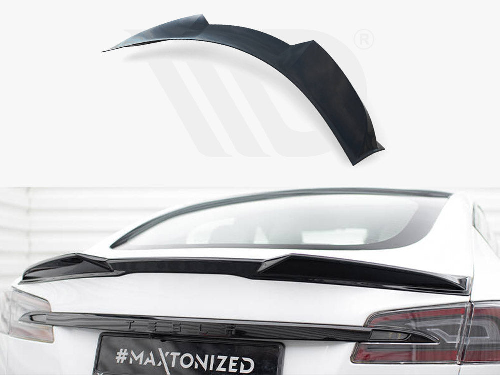 A black car spoiler is positioned on the rear of a white vehicle, with the text "#MAXTONIZED" on the license plate. It rests in a bright, indoor environment.