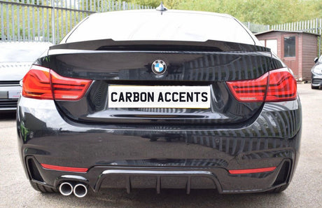 Car with dual exhaust displays "CARBON ACCENTS" on the license plate; parked on a paved surface with metal fencing and greenery in the background.