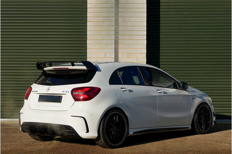 A white Mercedes A45 AMG car is parked outside, featuring a rear spoiler and dual exhausts. It's situated against a background of green horizontal metal shutters.