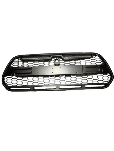 A black car grille with a hexagonal mesh pattern rests against a white background. The center features a circular cutout at the top part for a logo or emblem.
