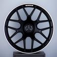 A black alloy wheel with a Mercedes emblem and "AMG" text, mounted vertically on a display stand against a plain gray background.