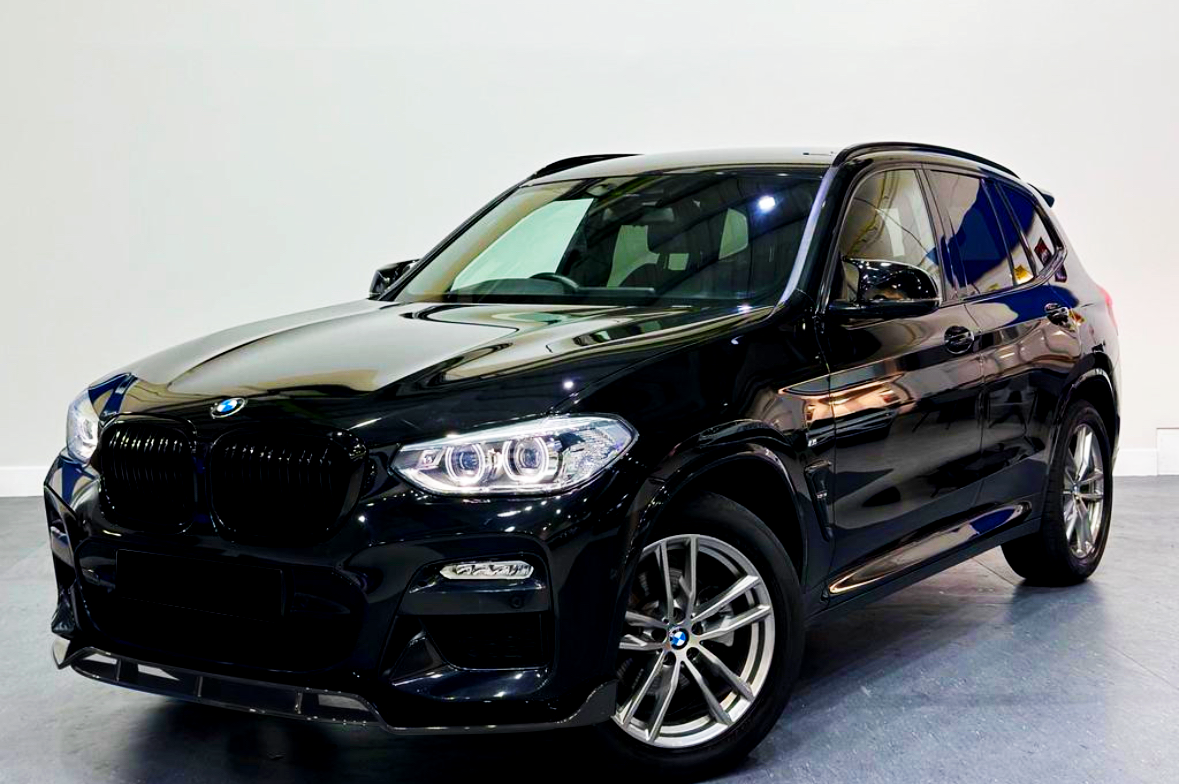 A shiny black SUV is parked indoors, featuring alloy wheels and illuminated headlights, set on a smooth gray floor against a plain white wall.