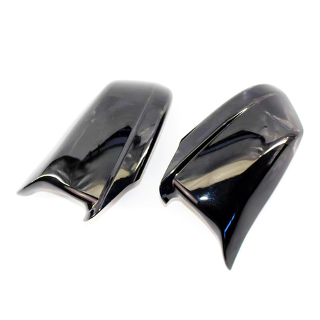 Two glossy black plastic car mirror covers, positioned side by side, reflecting light on a plain white background.