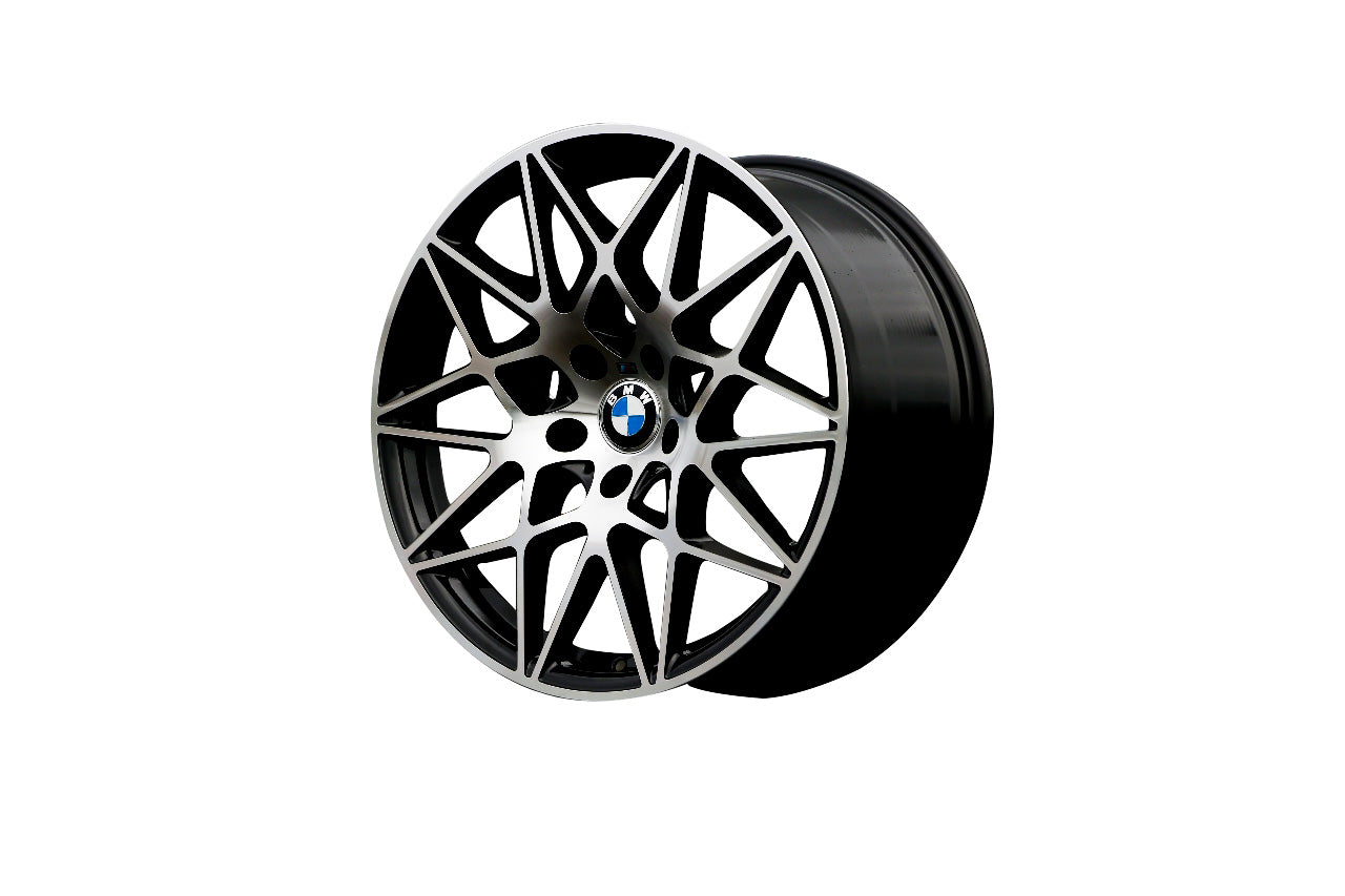 A multi-spoke car wheel, displaying a BMW emblem at the center, rests against a plain white background. Its intricate design combines silver spokes with black detailing.