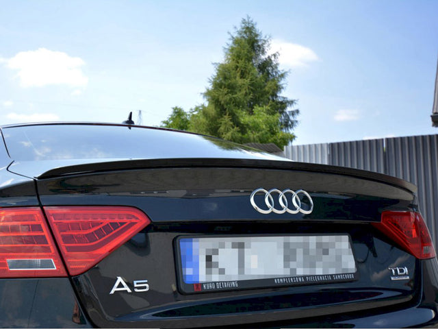 The rear of a black Audi A5 displays its logo and taillights, parked outdoors. Plate text reads: "Kuro Detailing Kompleksowa Pielęgnacja Samochodu." Trees and a fence are visible.