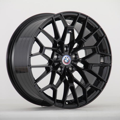 A shiny black alloy wheel with a geometric, multi-spoke pattern displays the BMW logo at its center. It rests upright on a plain white background.