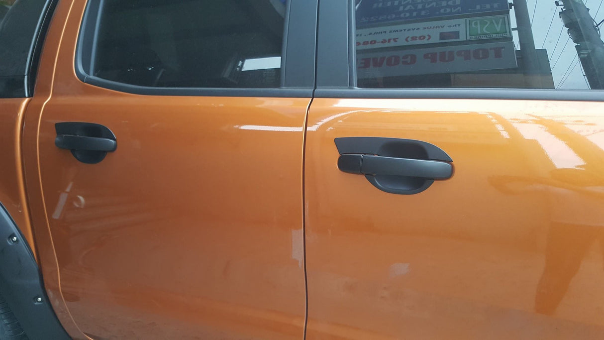 Orange car doors with black handles are closed, reflecting nearby objects. A sign with text is visible through the window.