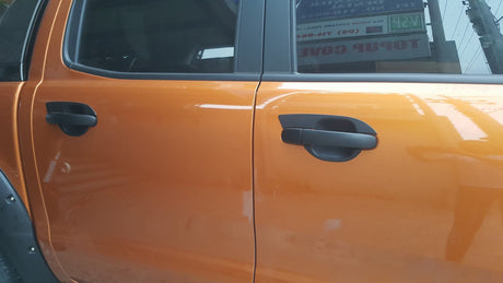 Orange car doors with black handles are closed, reflecting nearby objects. A sign with text is visible through the window.