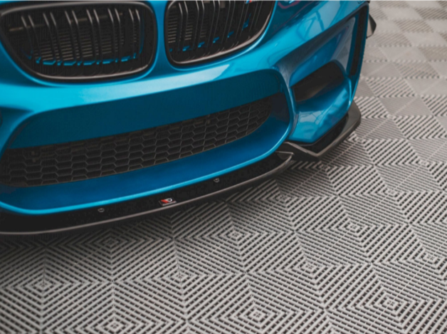 A blue car with a sporty front bumper rests on a patterned floor, featuring a geometric design of interlocking diamond shapes.