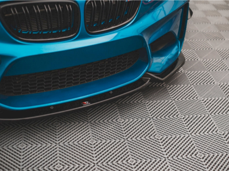 A blue car with a sporty front bumper rests on a patterned floor, featuring a geometric design of interlocking diamond shapes.