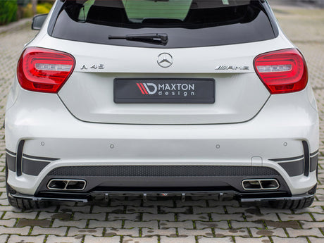 A white Mercedes A 45 AMG car is parked on a cobblestone surface, featuring a Maxton Design rear bumper and dual exhaust outlets.