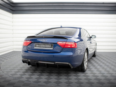 Blue Audi A5 parked in a garage with checkered flooring and white walls. The rear view shows a "#MAXTONIZED" license plate.