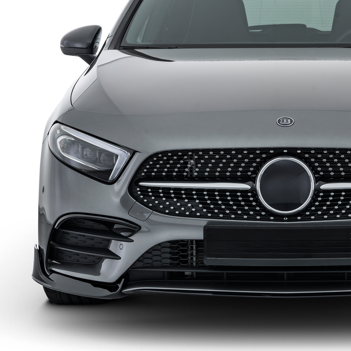 A gray luxury car is parked, showcasing its sleek front grille with a circular emblem. The vehicle sits in a well-lit studio environment, highlighting its polished exterior.