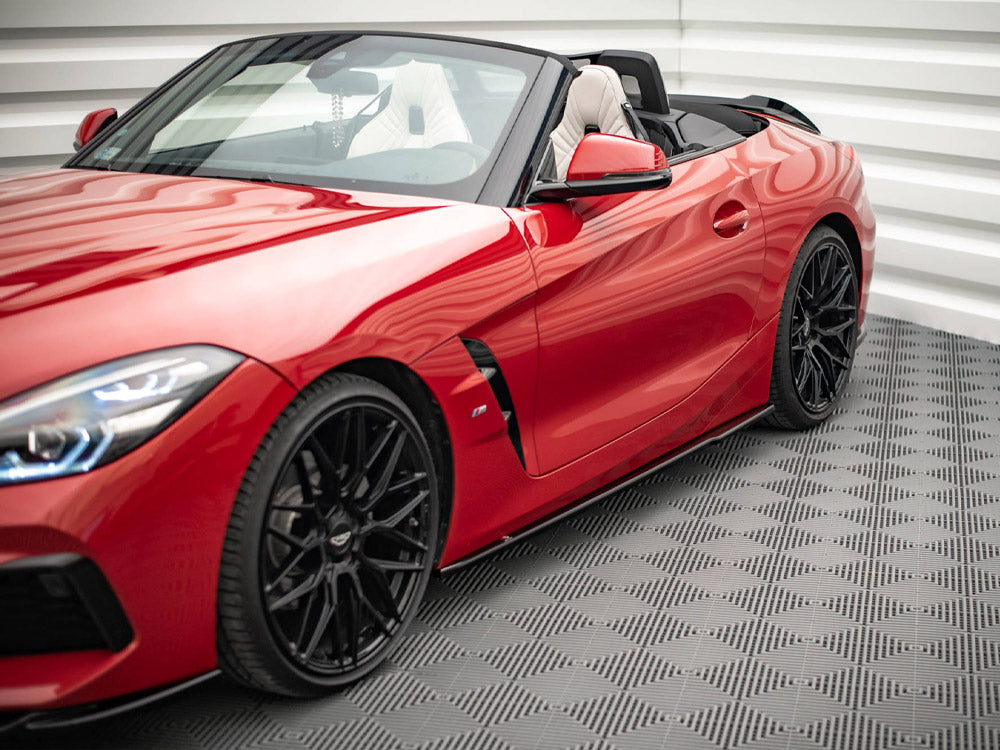 Red convertible sports car, parked with the top down, featuring sleek black wheels, in a bright, tiled space with geometric patterns on the floor and walls.