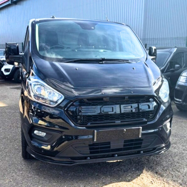 A black van with prominent front grille reading "BORD" is parked in an outdoor lot, surrounded by other vehicles and adjacent to a large building.