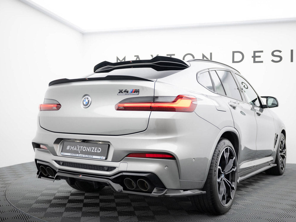 A silver BMW X4 M, featuring a rear spoiler and quad exhausts, is stationary on a checkered platform. Visible text includes "X4 M competition" and "#MAXTONIZED". It's in a showroom with "MAXTON DESIGN" partially visible on the wall.