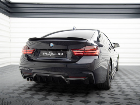 A sleek black BMW is parked in a modern, well-lit garage. The car, seen from the rear, features the text "#MAXTONIZED" on its license plate.
