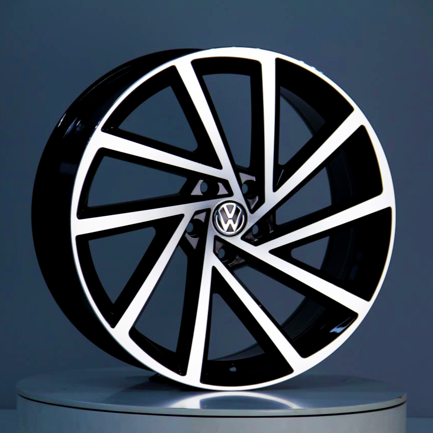 A black and white alloy wheel, featuring a Volkswagen logo in the center, stands on a round podium against a gray background.