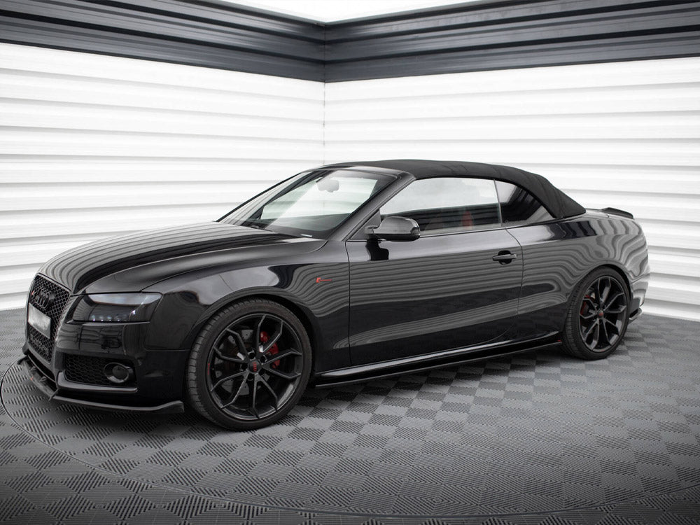 A sleek black convertible car with a soft top is parked in a modern, brightly lit, white-paneled showroom with a checkered floor.