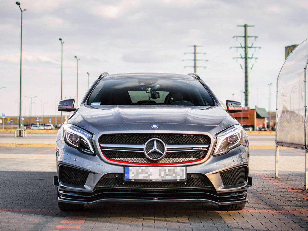 A silver Mercedes-Benz car is parked on a paved area. The setting is an open parking lot with utility poles and a cloudy sky in the background.