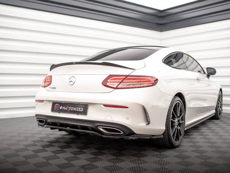 A white Mercedes-Benz C-Class coupe is stationary, displayed in a well-lit showroom with checkered flooring. The license plate reads "#MAXTONIZED."