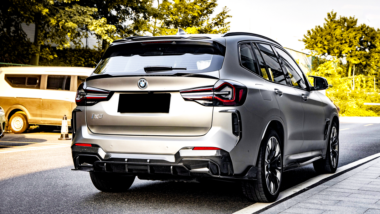 The object is a silver BMW iX3 SUV parked on a city street. It features distinctive taillights and a black license plate. Trees and other vehicles are nearby.