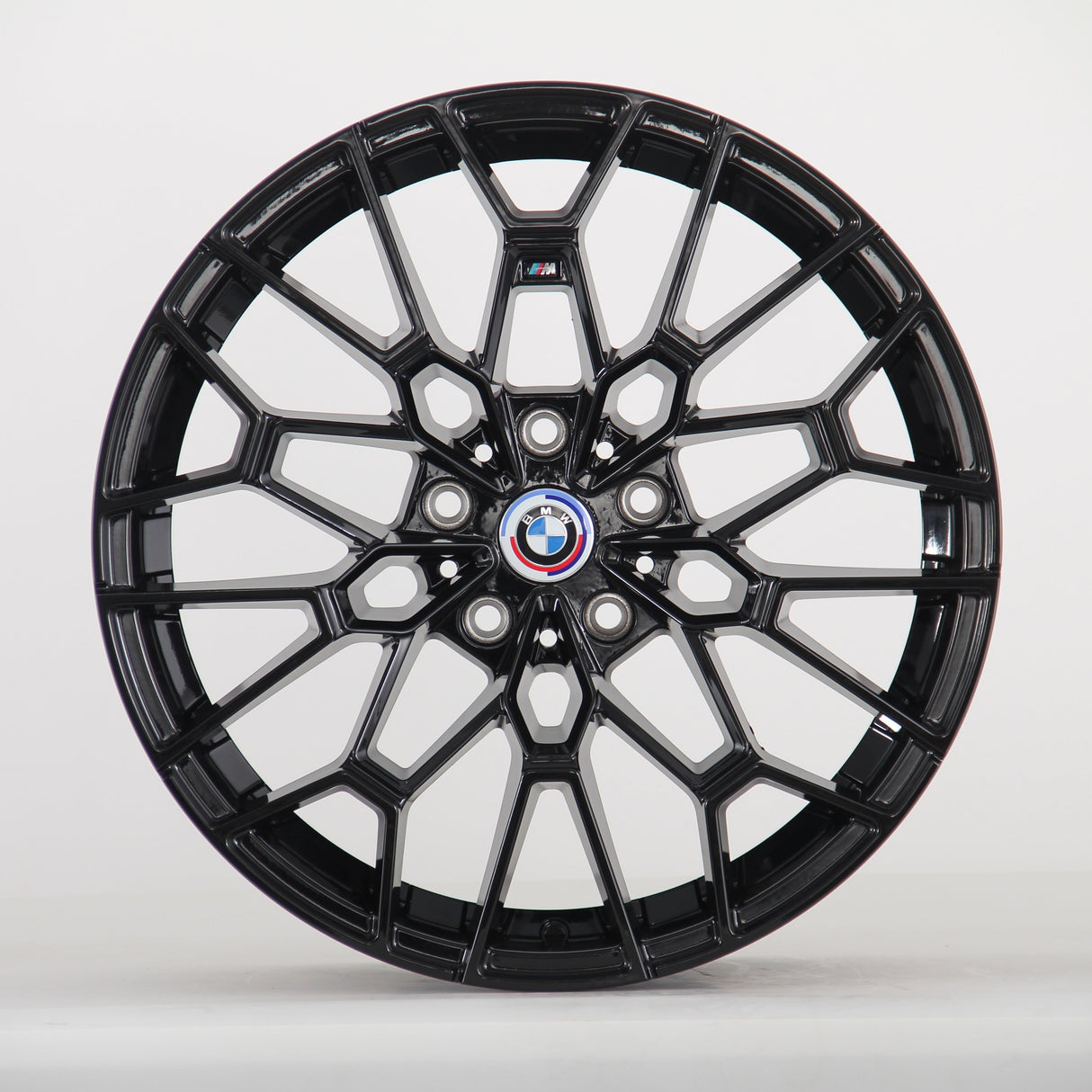 The image shows a black alloy wheel with a complex geometric design, featuring a blue, white, and red BMW logo at the center. The wheel is set against a plain white background.