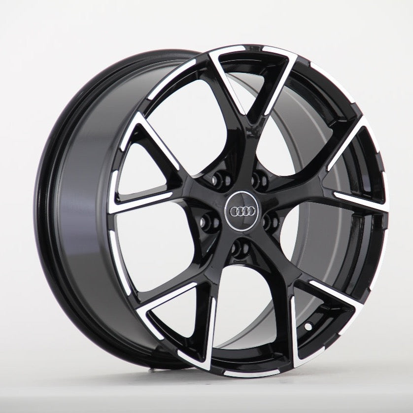 A black and silver Audi wheel rim with a five-spoke design is displayed against a plain white background. The Audi logo is centered on the wheel hub.