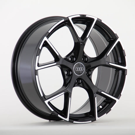 A black and silver Audi wheel rim with a five-spoke design is displayed against a plain white background. The Audi logo is centered on the wheel hub.