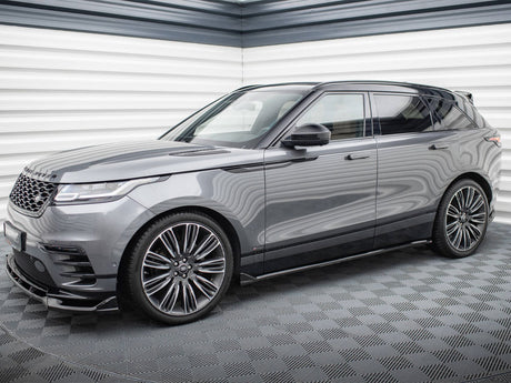 A sleek gray SUV is parked in a modern showroom with textured walls. It's a Range Rover, featuring large alloy wheels and a stylish, streamlined design.