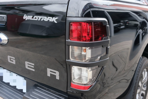 The truck's rear features a black tailgate with "WILDTRAK" and "RANGER" text, and a red and white tail light. It's parked on a paved surface with blurred surroundings.