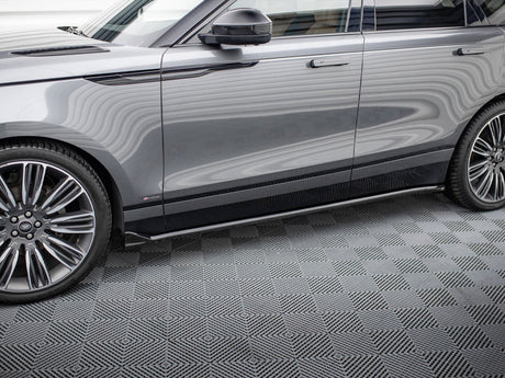A gray SUV is parked indoors on a patterned floor. The vehicle's shiny surface reflects wavy lines, a black handle is visible, and large chrome wheels dominate the foreground.